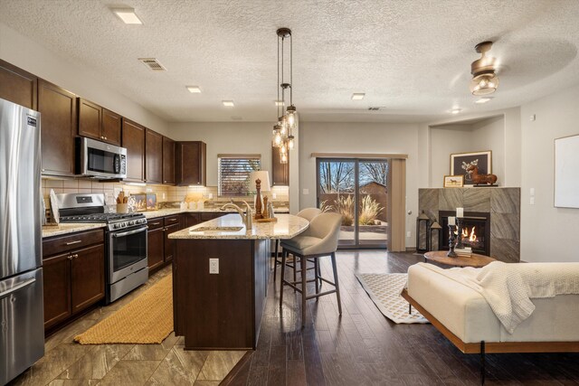 kitchen with stainless steel appliances, dark wood-type flooring, a high end fireplace, decorative backsplash, and a kitchen bar