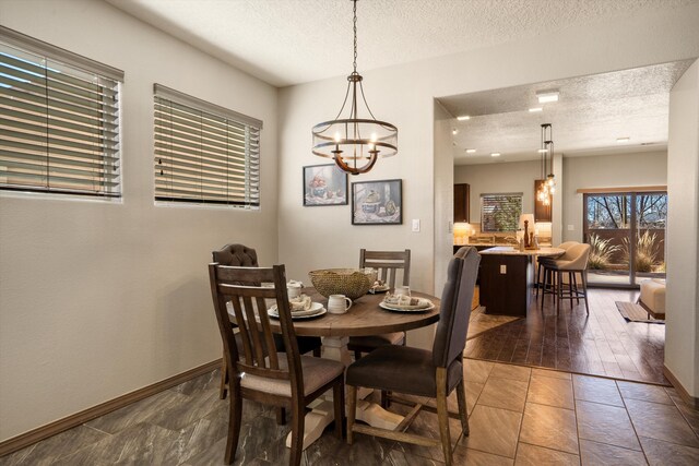 tiled dining space with a textured ceiling, an inviting chandelier, and baseboards