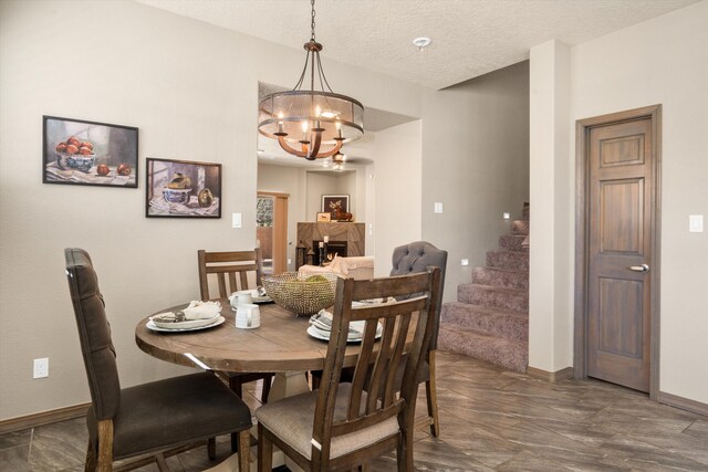 dining area featuring a warm lit fireplace, a textured ceiling, a chandelier, baseboards, and stairway