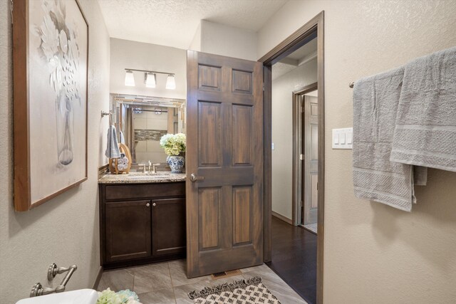 full bath with tile patterned flooring, a textured wall, a textured ceiling, and vanity