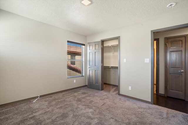 unfurnished bedroom with carpet flooring, a spacious closet, baseboards, and a textured ceiling