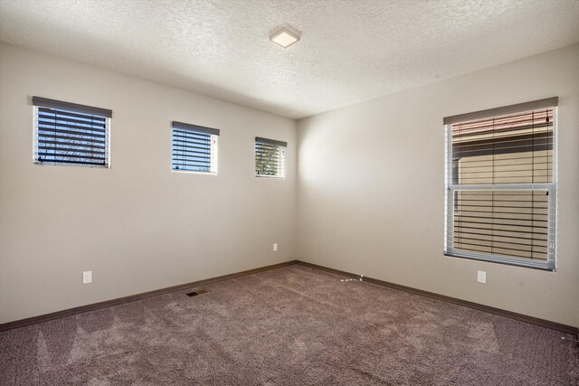 unfurnished room featuring a textured ceiling, carpet, visible vents, and baseboards