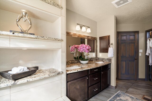 bathroom with a textured ceiling, double vanity, a sink, and visible vents