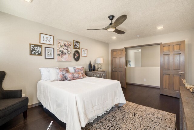 bedroom with a textured ceiling, ceiling fan, dark wood-type flooring, and baseboards