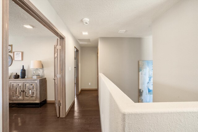 corridor with baseboards, a textured ceiling, an upstairs landing, and wood finished floors