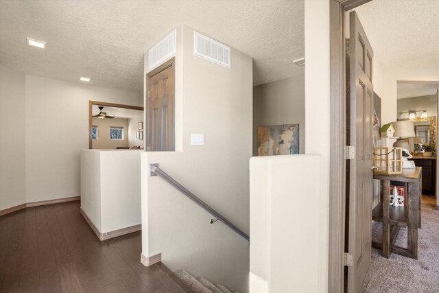 hallway with visible vents, a textured ceiling, wood finished floors, and an upstairs landing