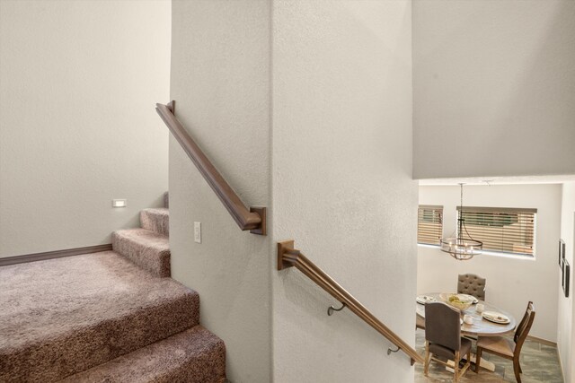 stairway featuring a chandelier, carpet flooring, and baseboards