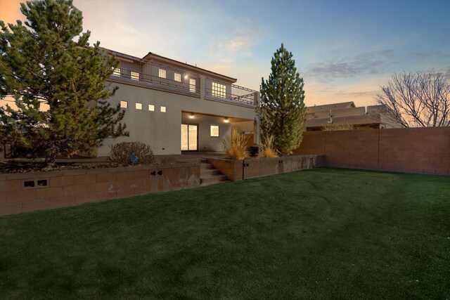 rear view of house featuring a yard, fence, a balcony, and stucco siding