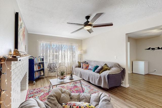 living room with a textured ceiling, a brick fireplace, wood finished floors, and a ceiling fan