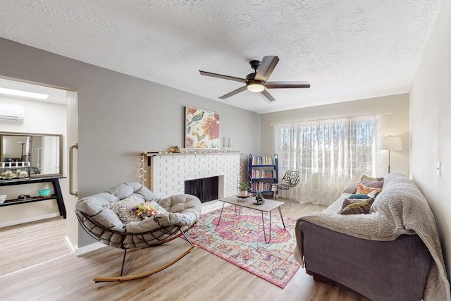 living room with a wall unit AC, a fireplace, ceiling fan, a textured ceiling, and wood finished floors