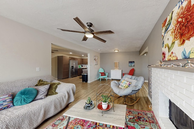 living area featuring a brick fireplace, light wood-style flooring, a ceiling fan, and a textured ceiling