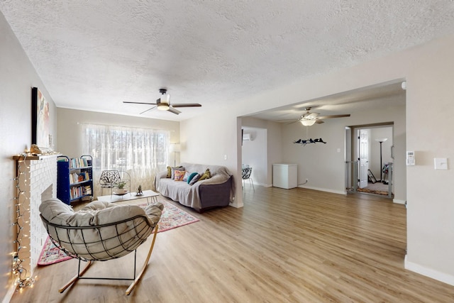 living area with a textured ceiling, ceiling fan, light wood-style flooring, and baseboards