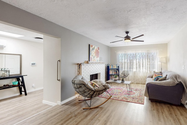 living room with a fireplace, wood finished floors, a ceiling fan, baseboards, and a wall mounted AC