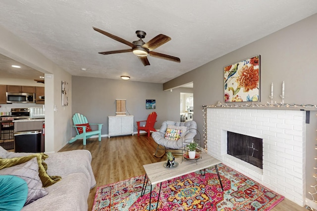 living room featuring a textured ceiling, ceiling fan, a brick fireplace, and wood finished floors