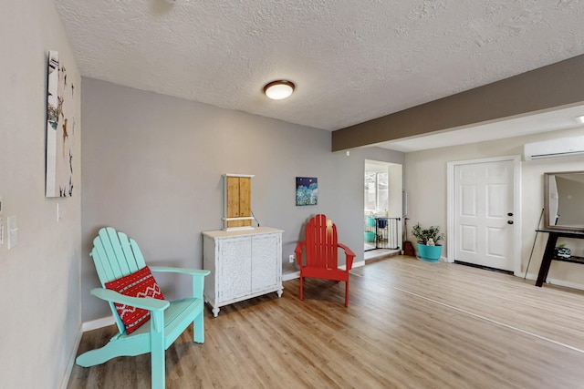 sitting room featuring light wood finished floors, baseboards, a textured ceiling, and a wall mounted AC