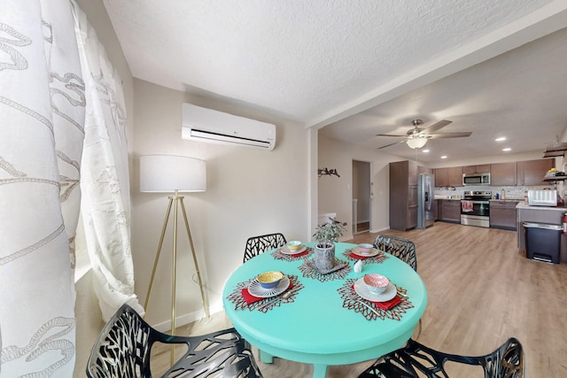 dining area with baseboards, ceiling fan, a textured ceiling, an AC wall unit, and light wood-type flooring