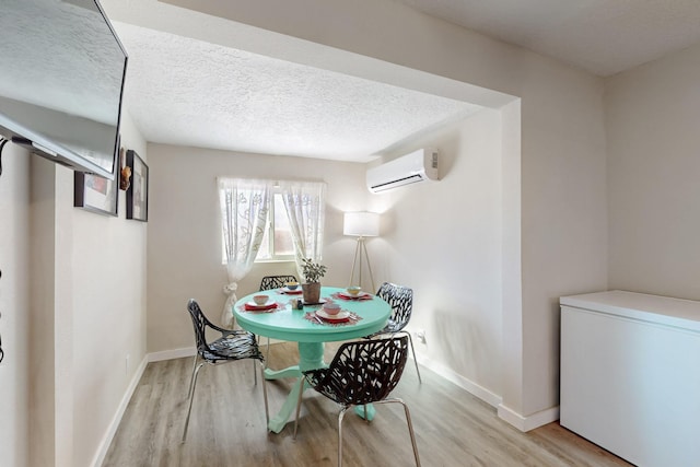 dining space featuring an AC wall unit, a textured ceiling, baseboards, and wood finished floors