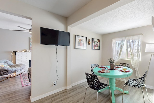 dining area with baseboards, ceiling fan, wood finished floors, a textured ceiling, and a brick fireplace