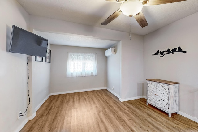 unfurnished room featuring ceiling fan, a textured ceiling, wood finished floors, baseboards, and a wall mounted AC