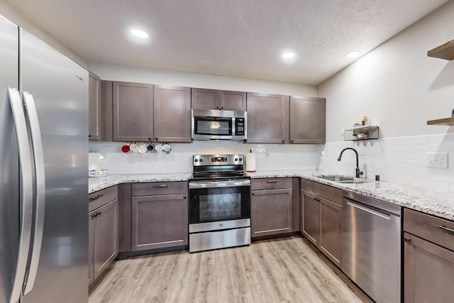 kitchen with light wood-style flooring, appliances with stainless steel finishes, light stone counters, a textured ceiling, and a sink