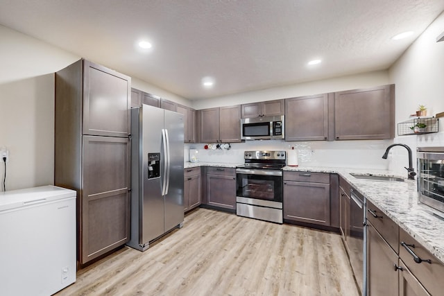 kitchen featuring light stone countertops, stainless steel appliances, light wood-type flooring, a sink, and recessed lighting