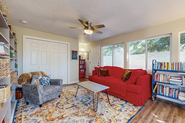 living room featuring ceiling fan, a textured ceiling, baseboards, and wood finished floors