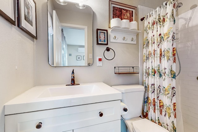 bathroom with toilet, a textured wall, a tile shower, and vanity