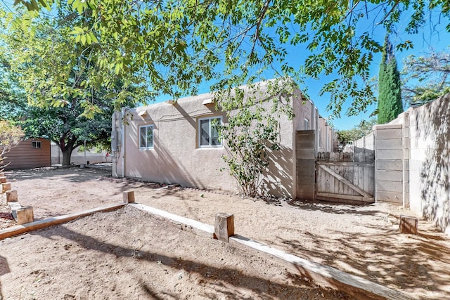 view of side of home featuring fence, a gate, and stucco siding