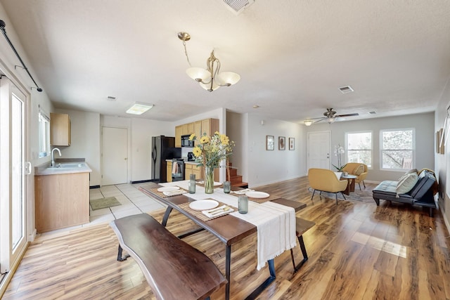 dining area featuring light wood-type flooring, visible vents, ceiling fan with notable chandelier, and stairway