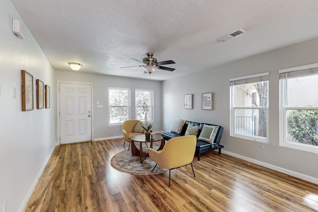 sitting room featuring visible vents, a ceiling fan, a textured ceiling, wood finished floors, and baseboards