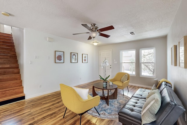 living area with visible vents, a ceiling fan, wood finished floors, stairway, and baseboards