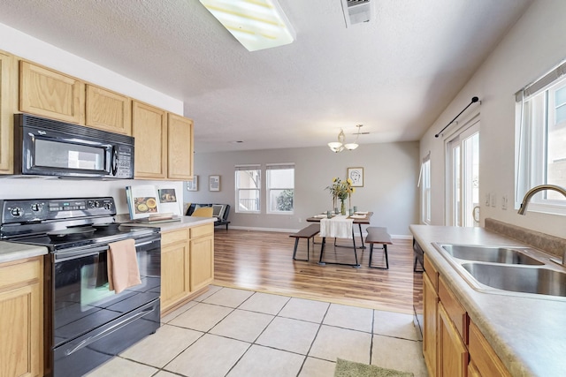 kitchen with light tile patterned floors, light brown cabinets, a sink, black appliances, and a textured ceiling