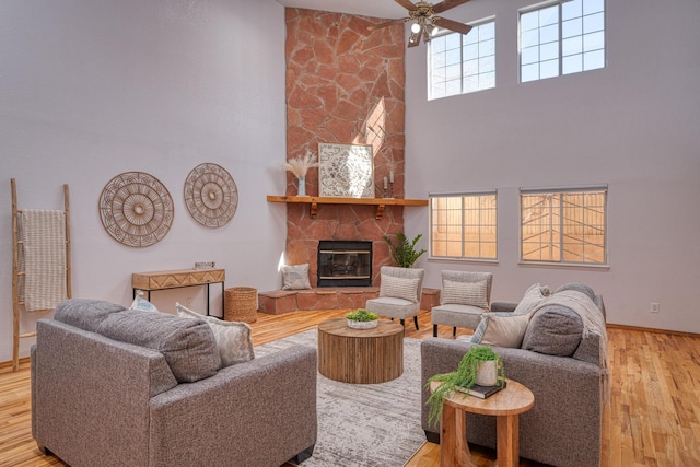 living area with a high ceiling, a fireplace, wood finished floors, a ceiling fan, and baseboards