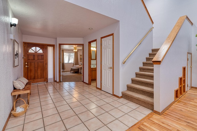 foyer featuring light tile patterned floors, a textured ceiling, baseboards, and stairs