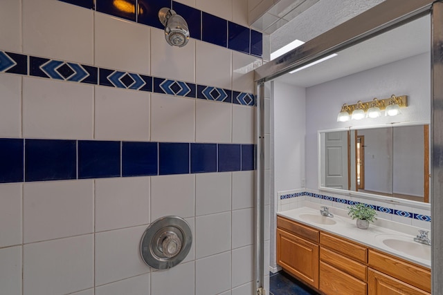 bathroom featuring double vanity, a tile shower, and a sink