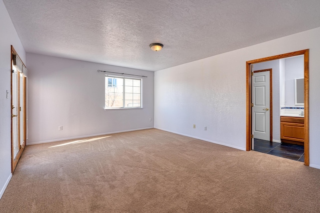 empty room with a textured ceiling, dark colored carpet, and baseboards