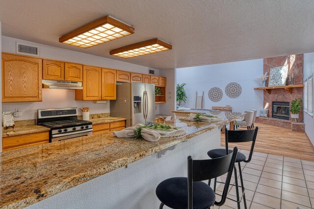 kitchen featuring light tile patterned flooring, under cabinet range hood, stainless steel appliances, visible vents, and a kitchen bar