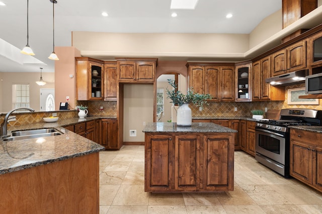 kitchen with dark stone counters, a kitchen island, appliances with stainless steel finishes, under cabinet range hood, and a sink