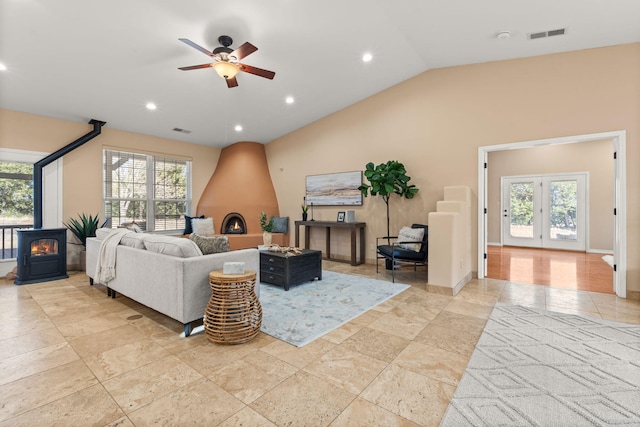 living area featuring vaulted ceiling, a wood stove, visible vents, and plenty of natural light