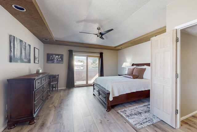 bedroom featuring a textured ceiling, baseboards, access to exterior, light wood finished floors, and a raised ceiling