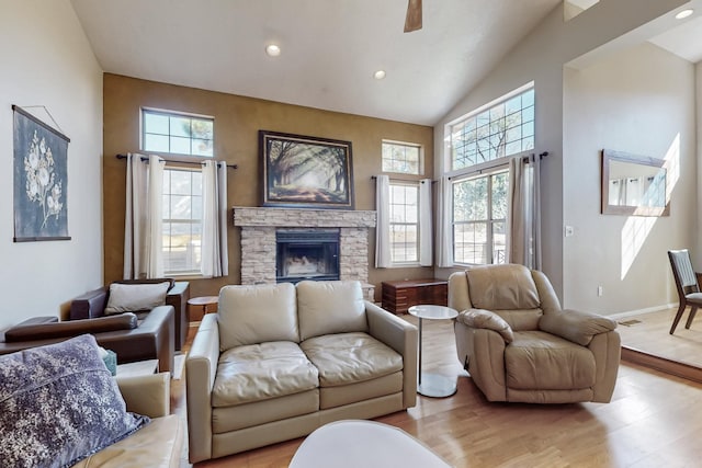 living area featuring baseboards, light wood-style flooring, a stone fireplace, high vaulted ceiling, and recessed lighting