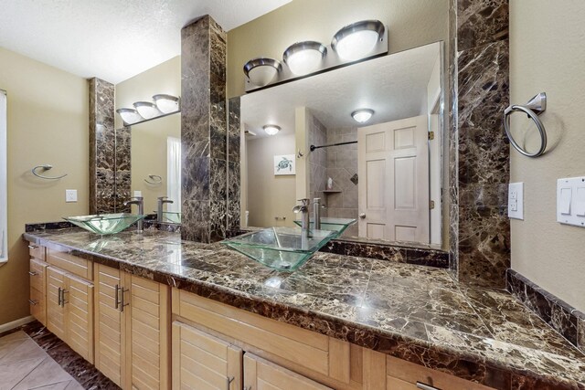 full bathroom featuring a tile shower, double vanity, tile patterned flooring, and a sink