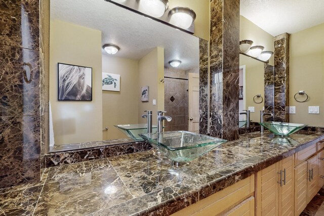 bathroom with a stall shower, a sink, a textured ceiling, and double vanity