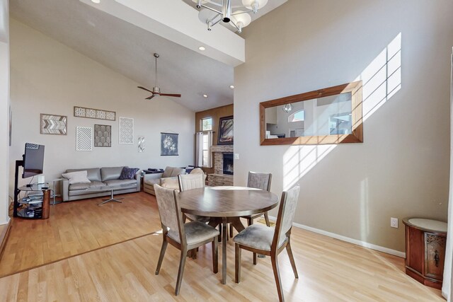 dining room with a fireplace, light wood-style flooring, ceiling fan, high vaulted ceiling, and baseboards