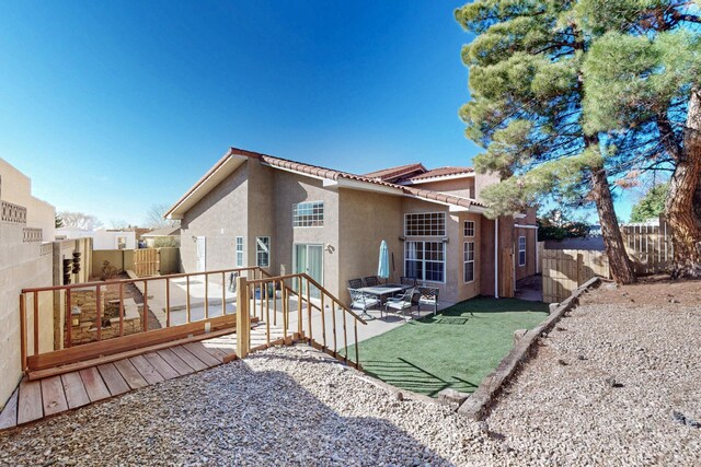 rear view of house featuring a fenced backyard, a tile roof, a wooden deck, and stucco siding