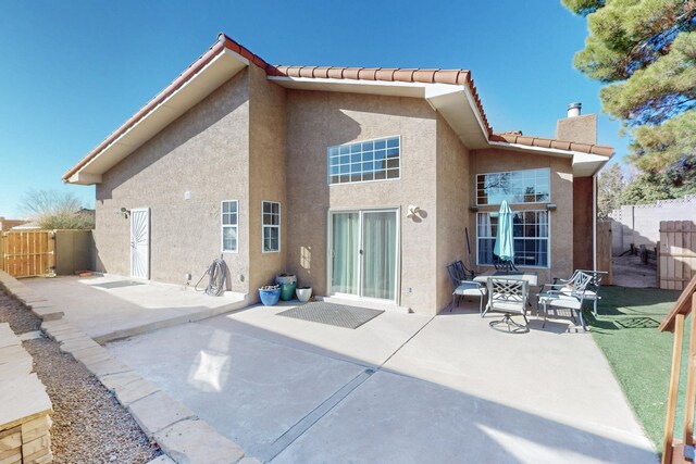 rear view of property featuring a patio, a chimney, a tiled roof, and stucco siding