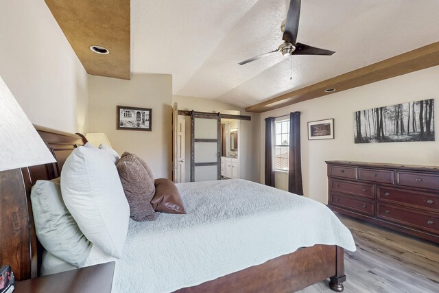 bedroom featuring lofted ceiling, a barn door, wood finished floors, and a ceiling fan