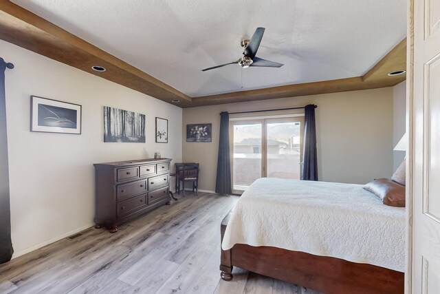 bedroom with light wood-type flooring, a raised ceiling, ceiling fan, and baseboards