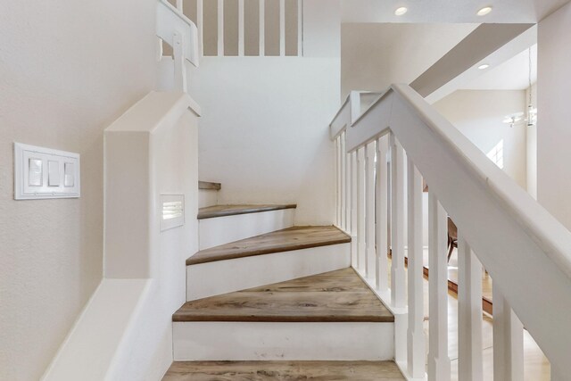 stairs featuring recessed lighting, a towering ceiling, and wood finished floors