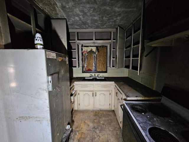 kitchen featuring white cabinets, electric stove, dark countertops, freestanding refrigerator, and a sink